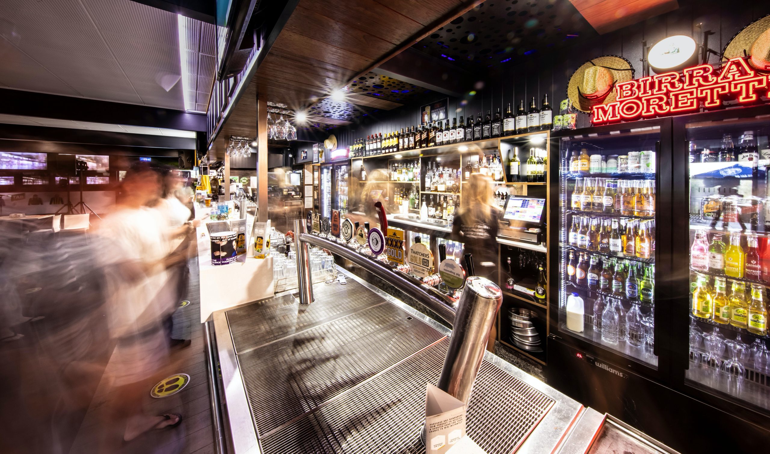 Night time view of the main bar and neon signs with long exposure blurring staff and customers
